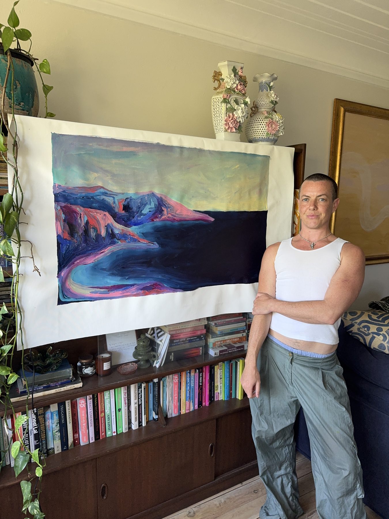 Dylin Hardcastle standing beside a large landscape painting in the studio