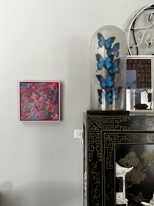 A small red square painting hung on a white wall